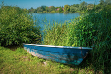 Blue Rowing Boat Lies On The Shore Of A Lake On Land