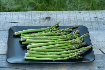 Fresh green asparagus spears in black plate on wooden table outdoor.