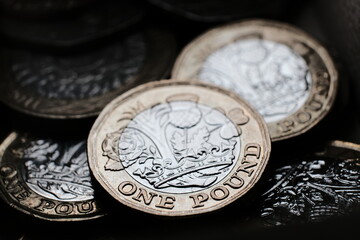 British one pound coins placed on top of each other in the box. Macro photo with dramatic shadows. 