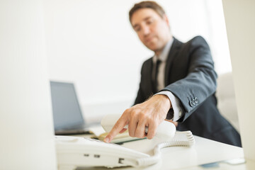 Wall Mural - Businessman sitting at his office desk dialing a telephone number