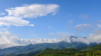 Wall Mural - Blue sunny landscape with some mountain clouds covering mountain peak in Montseny, Catalonia