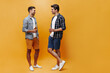 © Look! - Full-length portrait of brunet bearded men in shorts, white t-shirts and checkered shirts talking and holding beer bottles on orange background.