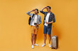 © Look! - Cheerful stylish travelers in white t-shirts, checkered shirts and colorful shorts look into distance and smile. Young men hold tickets and retro camera, pose with suitcase on orange background.