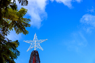 A star atop a Christmas tree, against the blue sky outdoors.