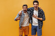 © Look! - Joyful brunet bearded men in colorful shorts, white t-shirts and checkered shirts laugh and point at camera on orange background.