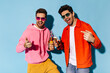 © Look! - Stylish happy young men in colorful sunglasses rejoice on blue background. Friends in bright outfits clink beer bottles.