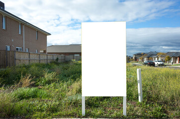 blank white empty mockup template of a real estate sign at front of a lot of vacant land on a suburb