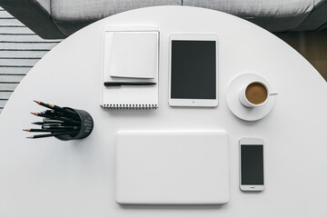 Modern laptop, tablet computer, mobile phone, cup of coffee and stationery on table in room
