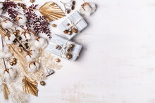 Gifts/Presents Decorated By Dried Flowers And Grasses Including; Cotton Flowers Or Stems, Gold Painted Palm Fronds, Ruscus Leaves, Wheat And Gum Nuts, On A Rustic White Background.