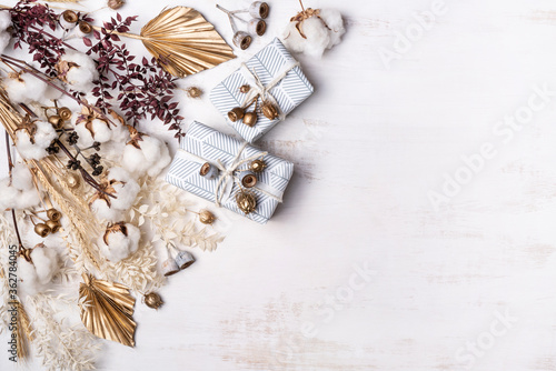 Gifts/Presents decorated by dried flowers and grasses including; Cotton flowers or stems, gold painted Palm fronds, Ruscus leaves, wheat and gum nuts, on a rustic white background.