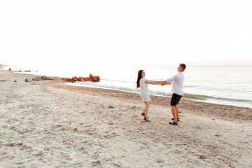 Wall Mural - Loving couple in white clothes during a honeymoon at sea walk on the sand at a photoshoot Love Story, ocean coast, beach
