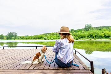 Wall Mural - Woman wearing straw hat and sunglasses while sitting on the pier with her puppy and relaxing