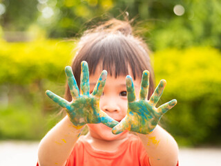 Cheerful little child girl with hands painted in colorful paints on nature background.