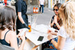 © Vadim Pastuh - Attractive girls spend time together in the summer terrace. The waiter brought cold soft drinks and is putting on the table, three young women sit and talk