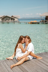 Wall Mural - Happy just married couple hug each other, sit on wooden pier during their vacation on Maldives island. Honeymoon concept