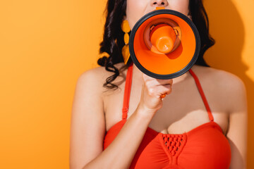 Wall Mural - cropped view of young woman screaming in megaphone on orange