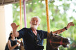 senior handsome elderly caucasian old man having fun with carousel  in the park outdoors, senior father laughed and smiled happily in the amusement park.