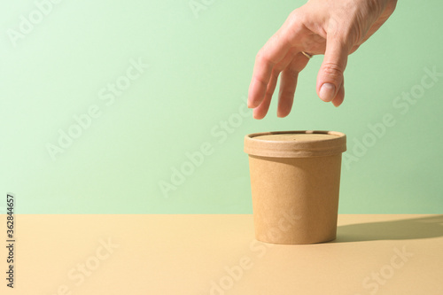 Craft paper soup cup and female hand on brown background. Ecological individual package. Zero Waste.