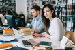 © BullRun - Long haired woman writing at table in library and looking at camera