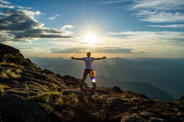 Canvas Print - Young male standing on top of a hill with his hands towards the sky at sunset- success concept