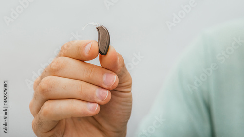 BTE hearing aid close-up in a male hand. Hearing solution, man holds a hearing aid, macro
