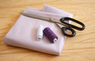 scissors and thread for sewing lie on a folded piece of fabric on the table