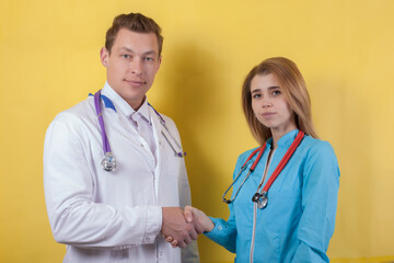 two doctors a man and a woman stand on a yellow background and shake hands .