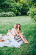 © alex - Outdoor countryside portrait of two happy sisters and best friends, enjoying picnic at vintage French style, stylish feminine outfits, tasty food and vine, nice time together. Summer time at nature