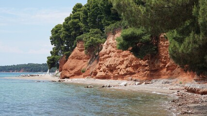 Canvas Print - Closeup shot of a cliff with orange soul and think green forests surrounded by sea waters