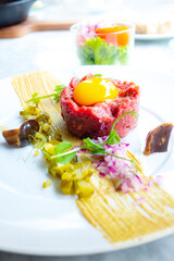 Wall Mural - Traditional beef tartar served with a raw egg on top, onion and cucumber in white plate ready to be eaten