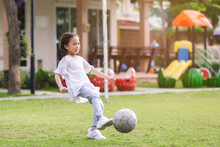 Asian Cute Baby Girl Wearing White Shirt Playing Football On Field Playground Merrily.