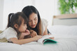 © linghaa - Love of young Asian mother and daughter. Teaching reading a homework or book on the white bed at home. daughter look the book and learning study at home felling be serious. Asian love family concept.