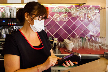 Waitress in a bar with a credit card terminal closing the card sale, mask by covid19