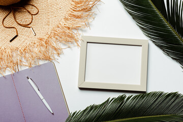 Canvas Print - top view of green palm leaves, square frame, violet notebook and sun hat on white background