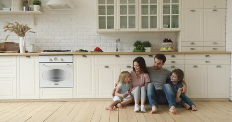 Wall Mural - Happy family mom dad and little cute children siblings talking laughing embracing sit on kitchen floor, smiling young parents having fun playing with funny small kids bonding together at home