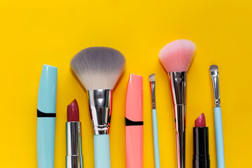 Wall Mural - Mascara, brushes and bright lipstick on a yellow background.
