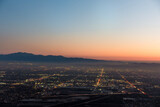 Fototapeta  - The city lights of the skyline of the Inland Empire near Los Angeles California begin to appear as the sun sets in a dramatic orange sunset. View from Potato Mountain in Claremont Wilderness Park