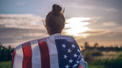 Portrait of a young beautiful woman in glasses and jeans with a waving American flag in her hands, background of blue sky, concept of patriotism, demonstration, protest.