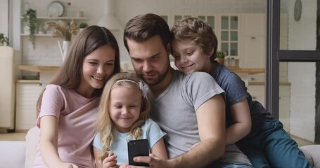 Wall Mural - Happy family parents with cute little kids children son daughter sit on sofa laugh having fun using smart phone funny social media app, take selfie, watching cartoons look at cellphone screen at home