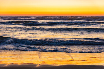 Wall Mural - Orange sunset glows in the sky and paints golden light across the waves and on wet sand on a beach in Oregon