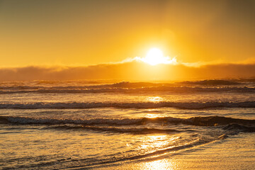 Wall Mural - Big orange sun at sunset lights up the sky and across the waves to the beach in golden glow