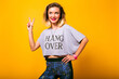 Young pretty woman wearing yoga bright sportive outfit, showing v gesture by her hand, hipster mood, yellow background.
