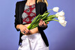 Close up image of woman holding bouquet of white tulips, violet background, stylish casual clothes, spring mood.