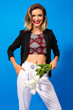 Elegant pretty woman posing at blue background, wearing suit and crop top, holding white tulips and smiling.