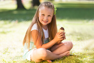 laughing child girl with ice cream sitting on grass in the park on a hot summer day