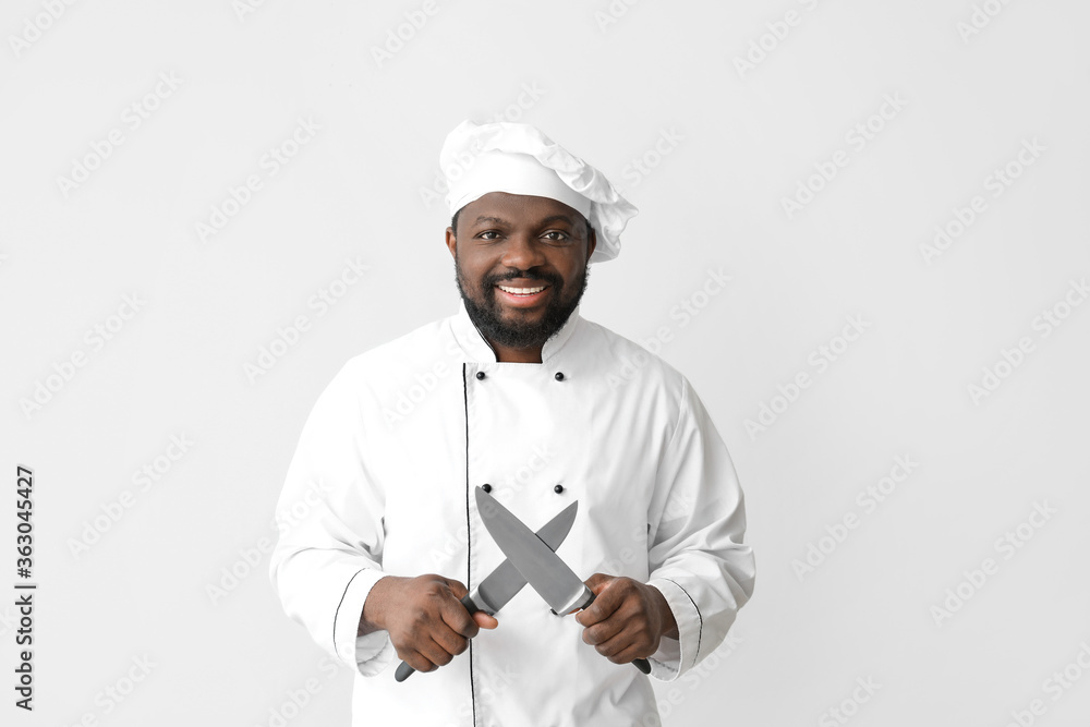 Male African-American chef with knives on white background