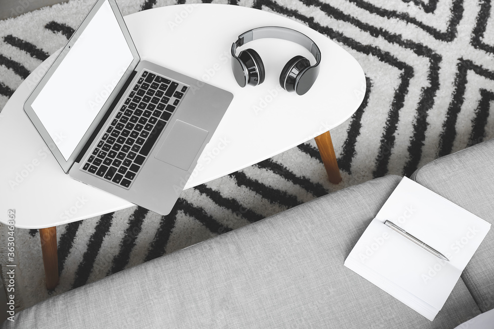 Modern laptop with headphones on table in room