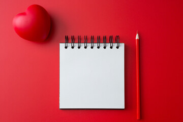 Wall Mural - Top view of Notebook, pencil, heart shaped ball  on a red background and copy space