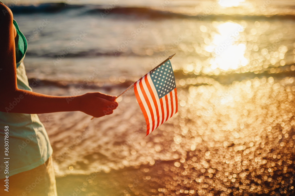 Midsection Of Person Holding American Flag Against Sea During Sunset - obrazy, fototapety, plakaty 