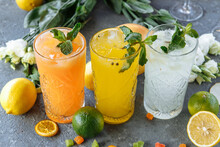 Summer fresh cold drink beverages. Ice Lemonade in the jug and lemons and orange with mint on the table outdoor. Orange lemonade in a glass